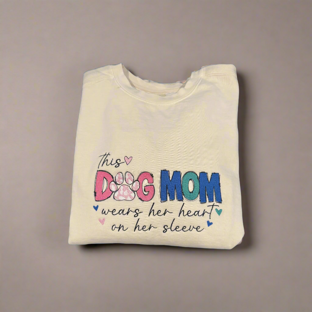 Folded beige sweatshirt with 'This Dog Mom wears her heart on her sleeve' text on a blue background