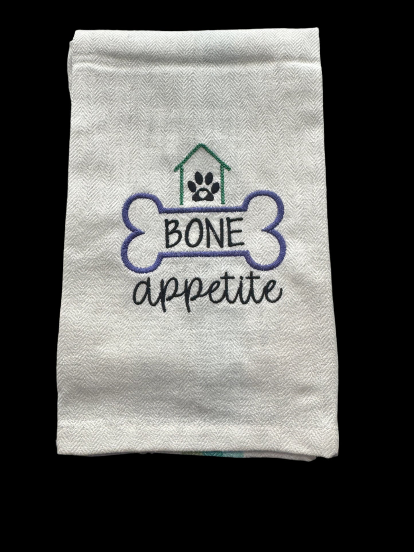 Folded white towel with 'Bone Appetite' embroidery on a grid background