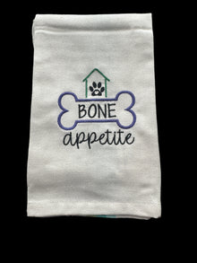 Folded white towel with 'Bone Appetite' embroidery on a grid background