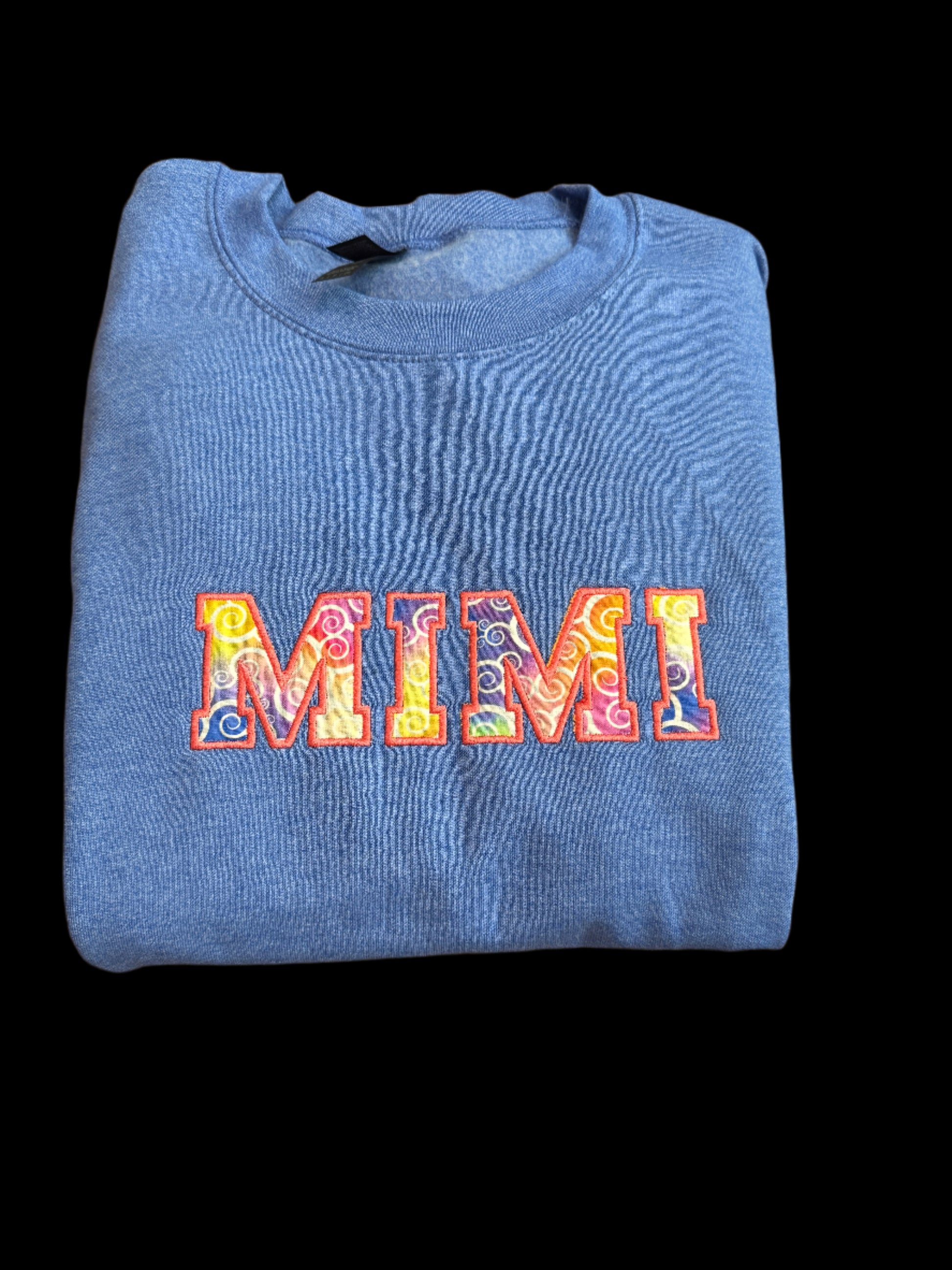 Folded blue sweatshirt with colorful text design on a woven surface