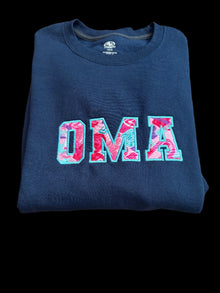 Folded navy blue sweatshirt with colorful 'OMA' text on a woven surface